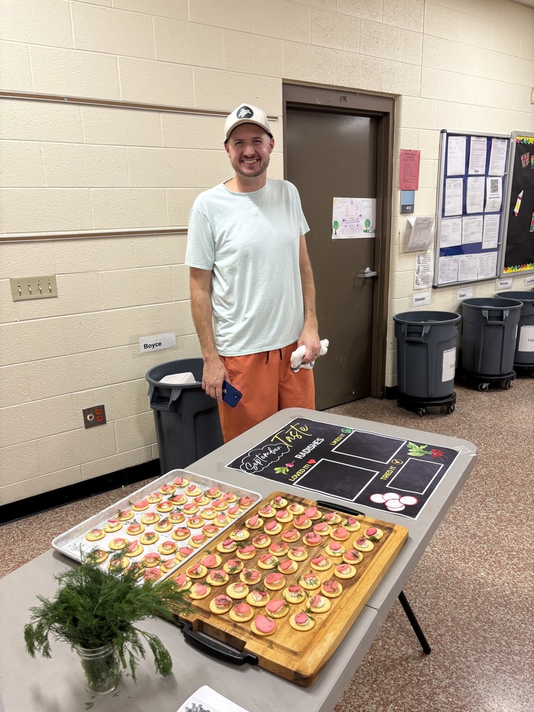 A person stands behind a table filled with small food items, a potted plant, and trays.