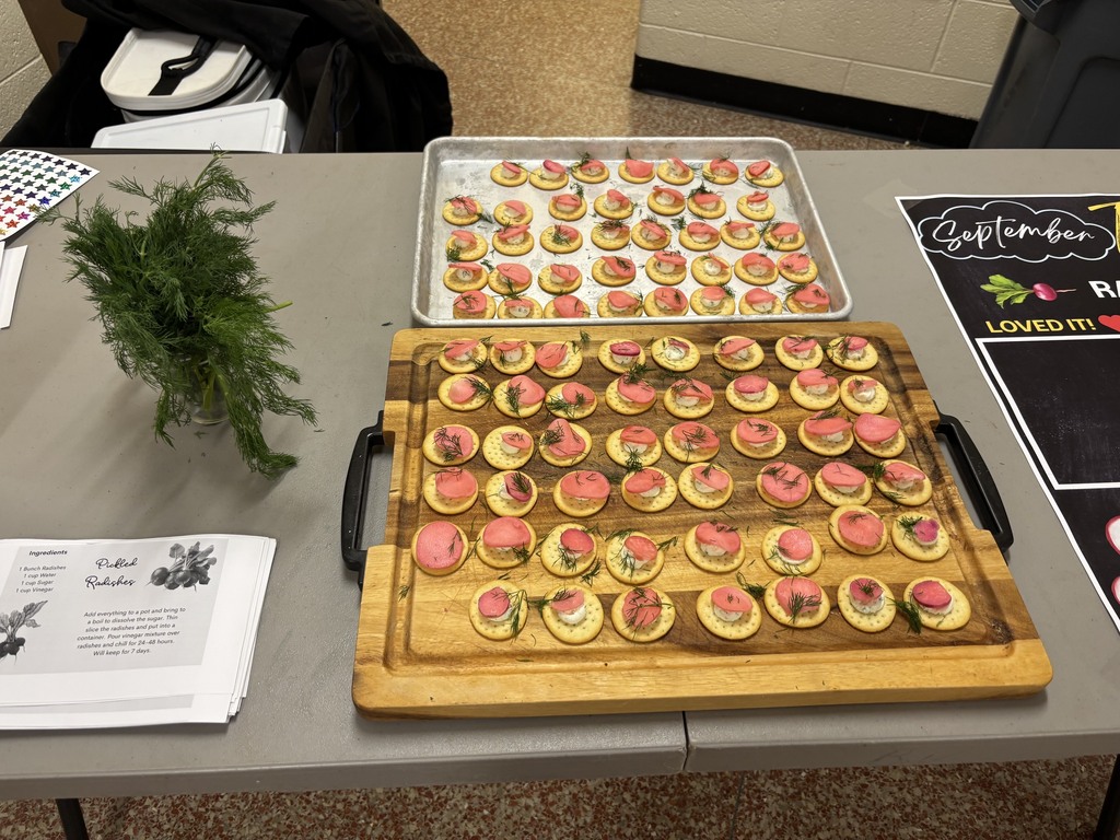 Two wooden trays of small, pink-topped appetizers on a table, along with a plant and papers.