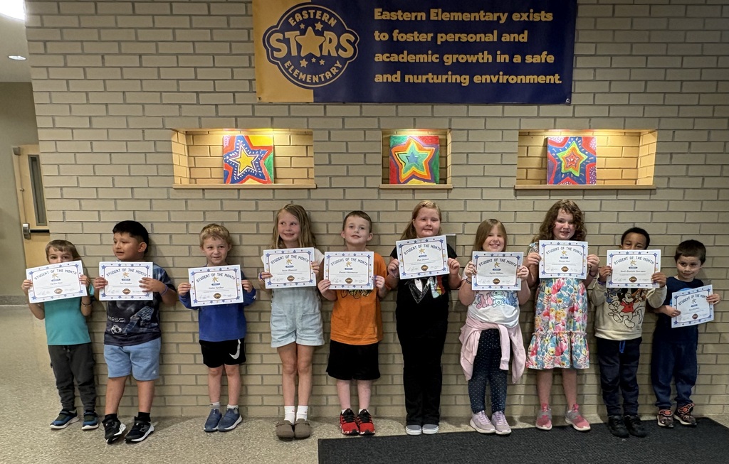 A group of children, all holding certificates, stand in a line in front of a brick wall.