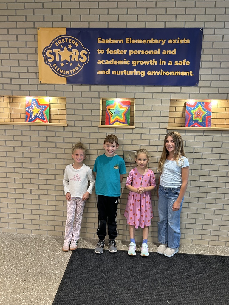 Four children stand before a brick wall. A sign behind them reads: "Eastern Elementary exists to foster personal and academic growth in a safe and nurturing environment."