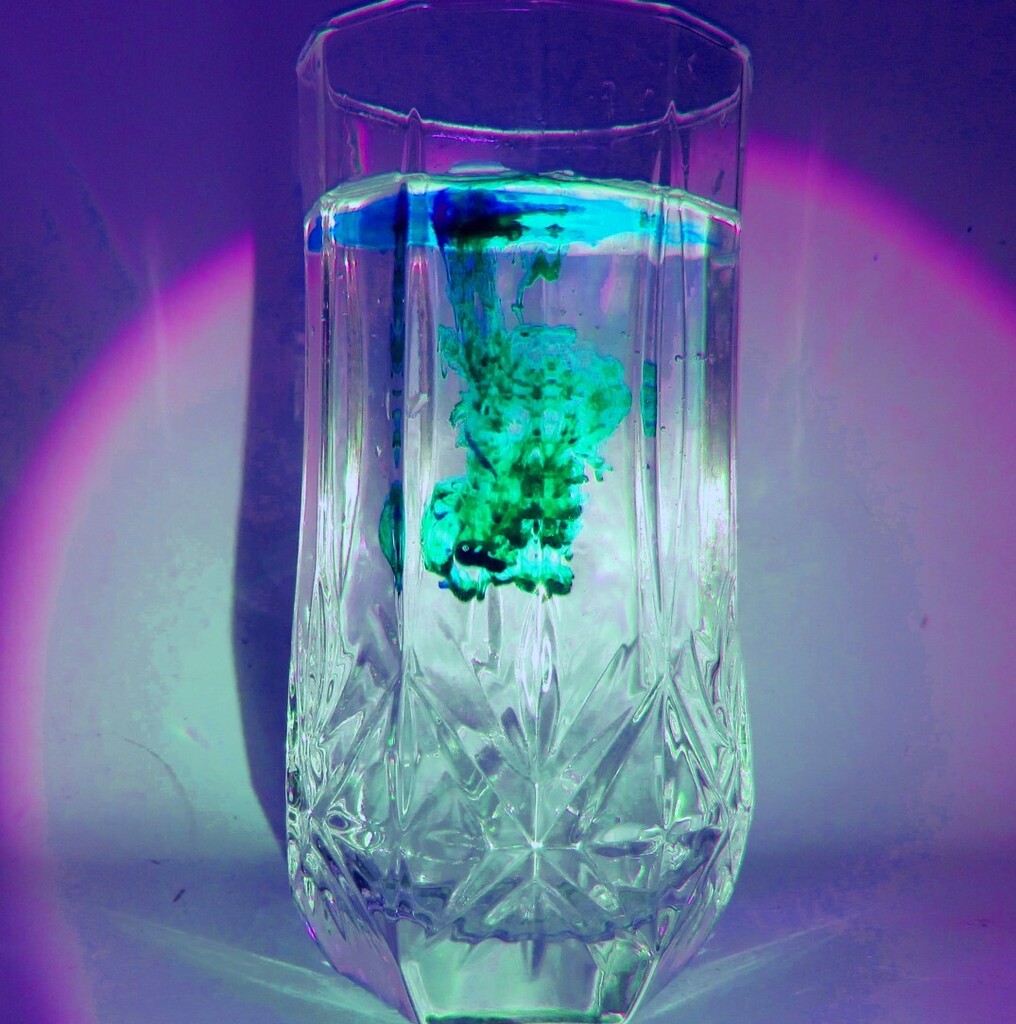 A glass with water and a green substance inside. Purple light in background.