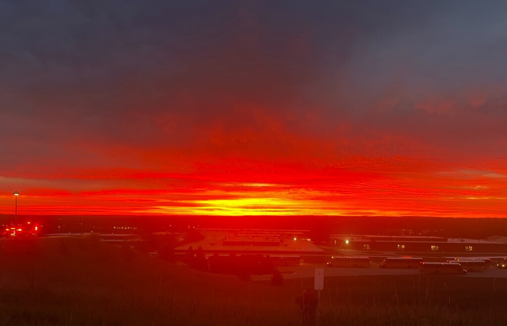 A sunset view from an elevated position showing a vibrant sky with orange and yellow hues, airport runways, and lights.