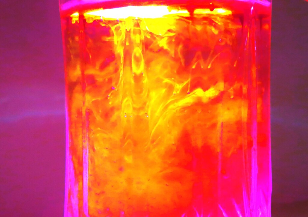 A glass container filled with glowing liquid, showing bright yellow and red colors against a purple background.