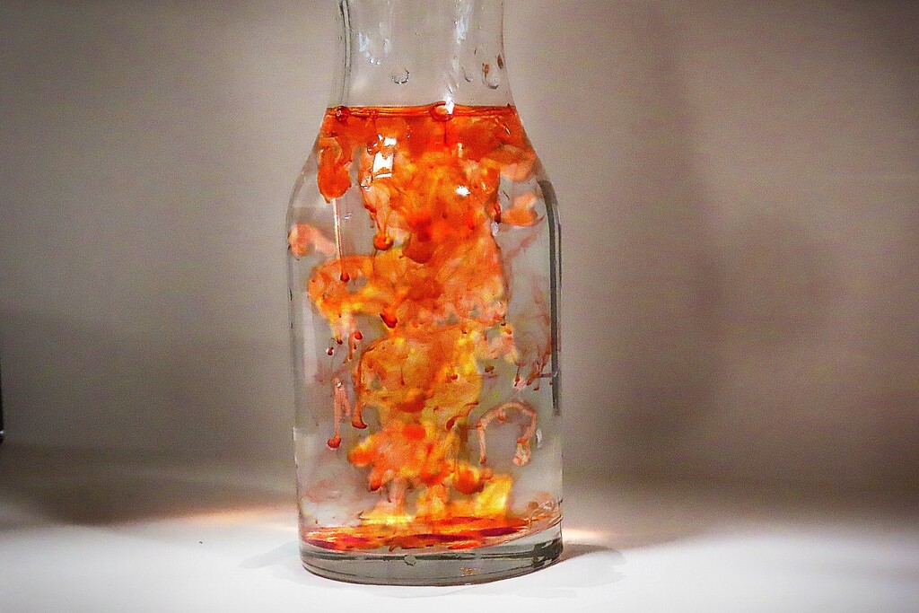 A bottle filled with orange liquid. The liquid swirls inside, resembling flowing flames against a plain white background.