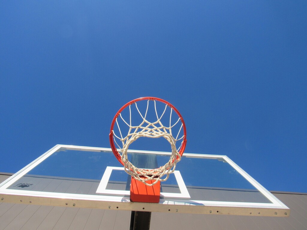 A basketball hoop with a red rim and net, backboard made of glass, and a black pole.