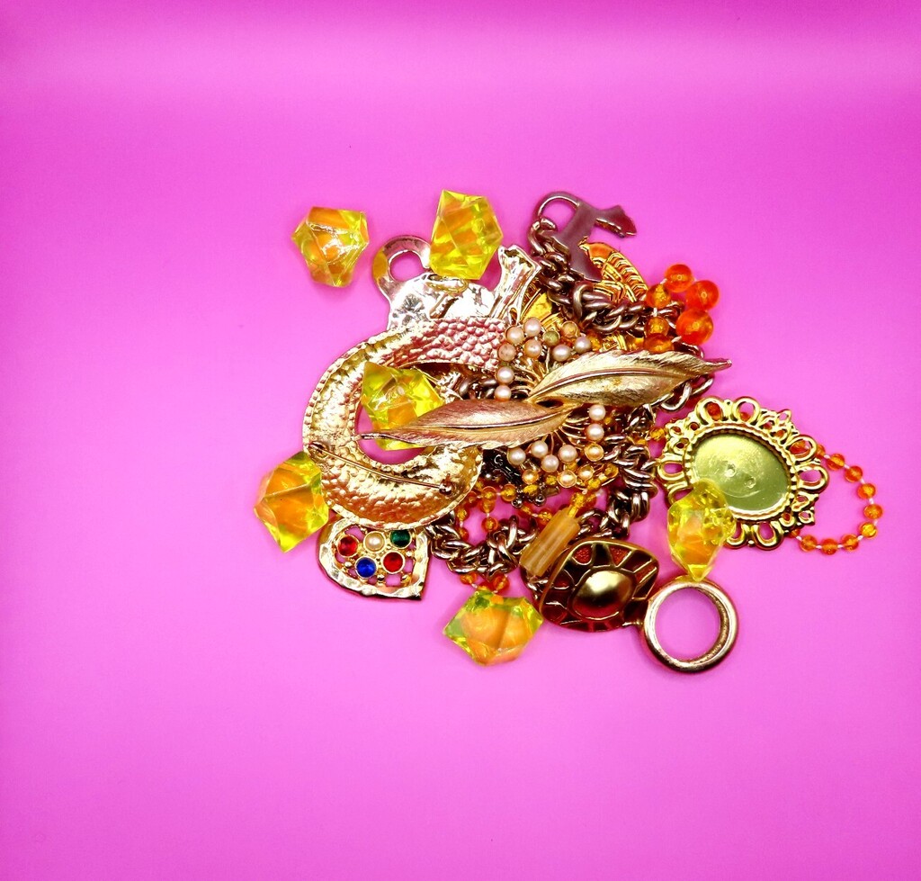 Various golden jewelry pieces, including rings, chains, and pendants with colorful stones, displayed on a bright pink background.