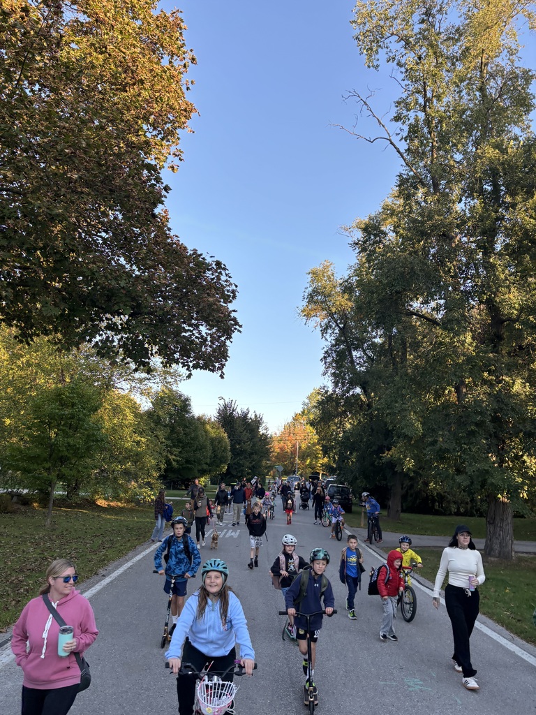 A group of people ride bicycles on a paved road, surrounded by trees with green and yellow leaves.