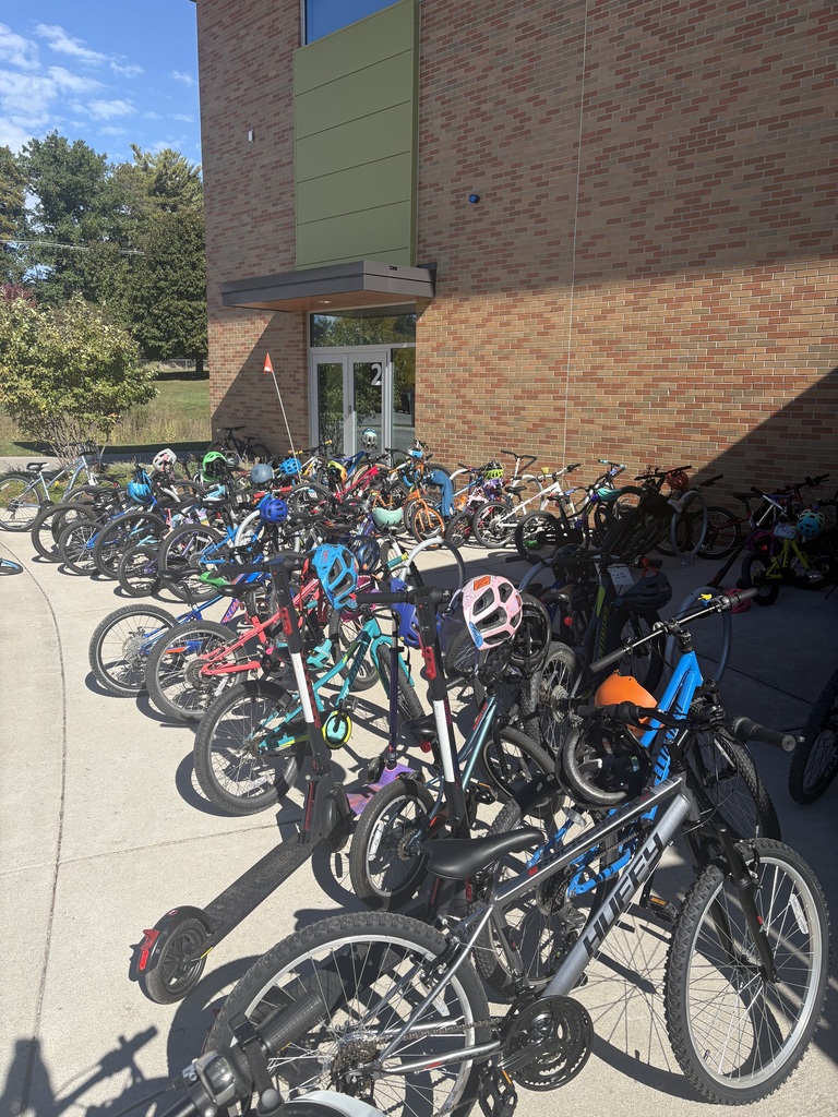 Bikes parked in a row outside a brick building with glass windows, next to trees.