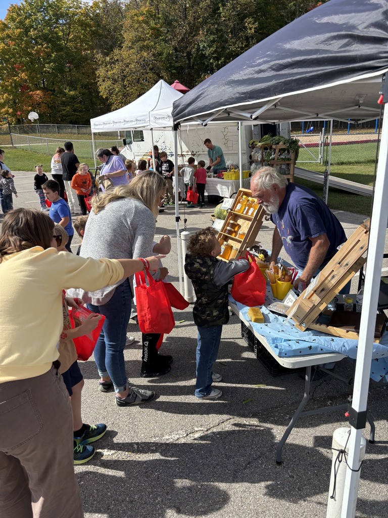 People gather around tents at an outdoor event, one man helps a child with a basket.