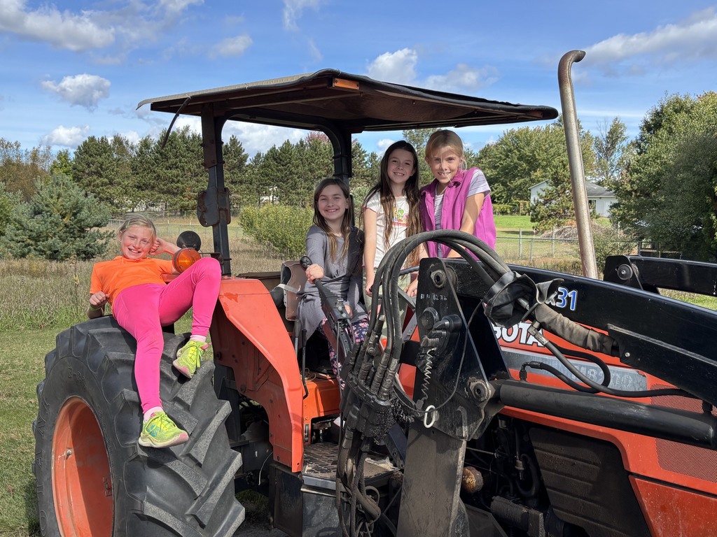 Four girls sitting on a red tractor; one girl is sitting on the front tire. Background contains trees.