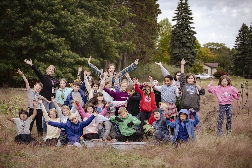 Group of children and adults posing together in a field with dry grass and trees.