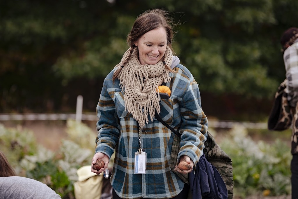 A woman wearing a plaid jacket and scarf walks through a garden with other people.