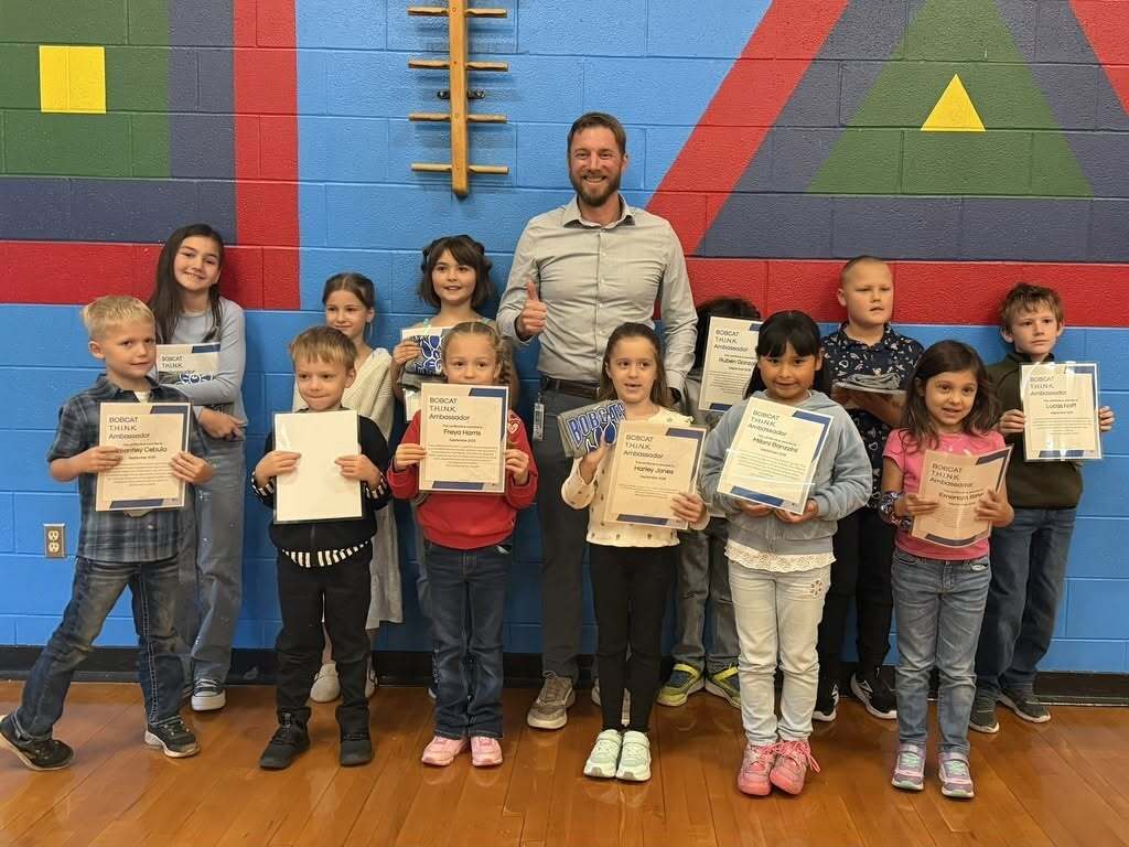 A group of young children holding certificates stands before a wall with colorful geometric designs.
