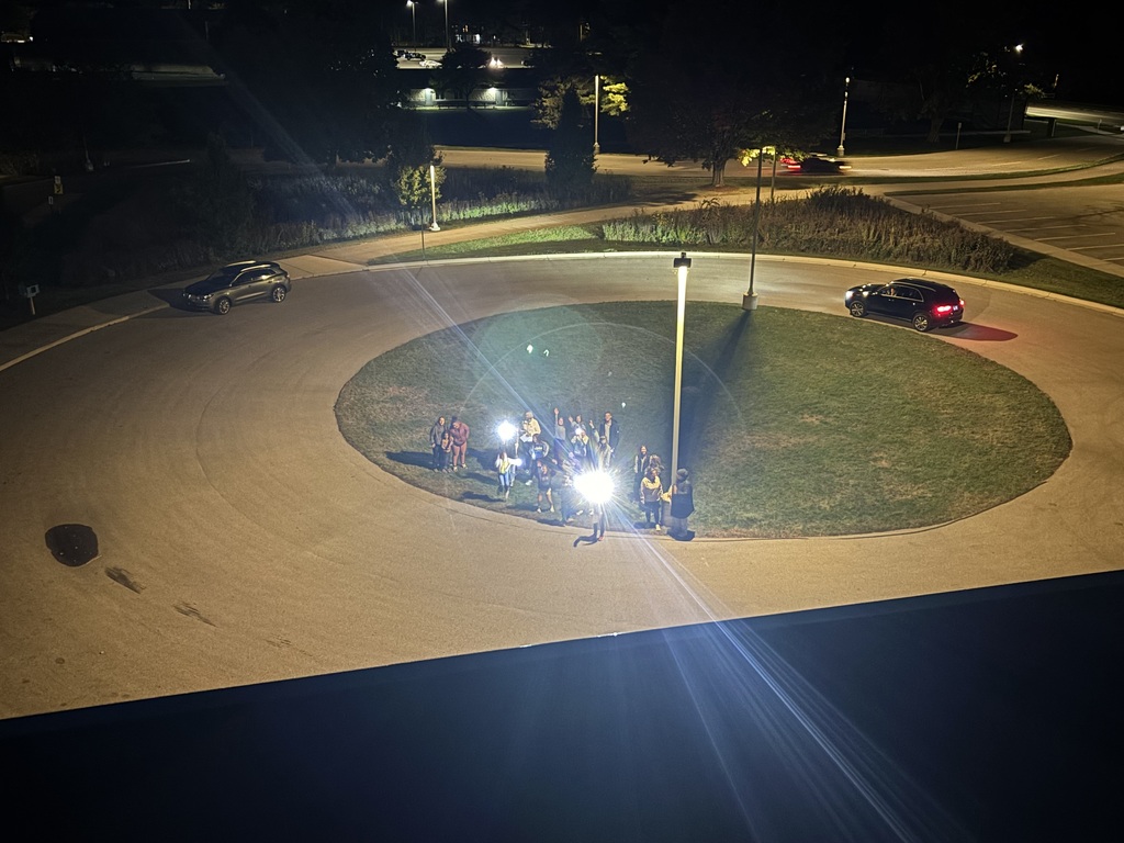 Roundabout with two cars and people with flashlights. People are waving up to Mr. Swegles on the school roof.