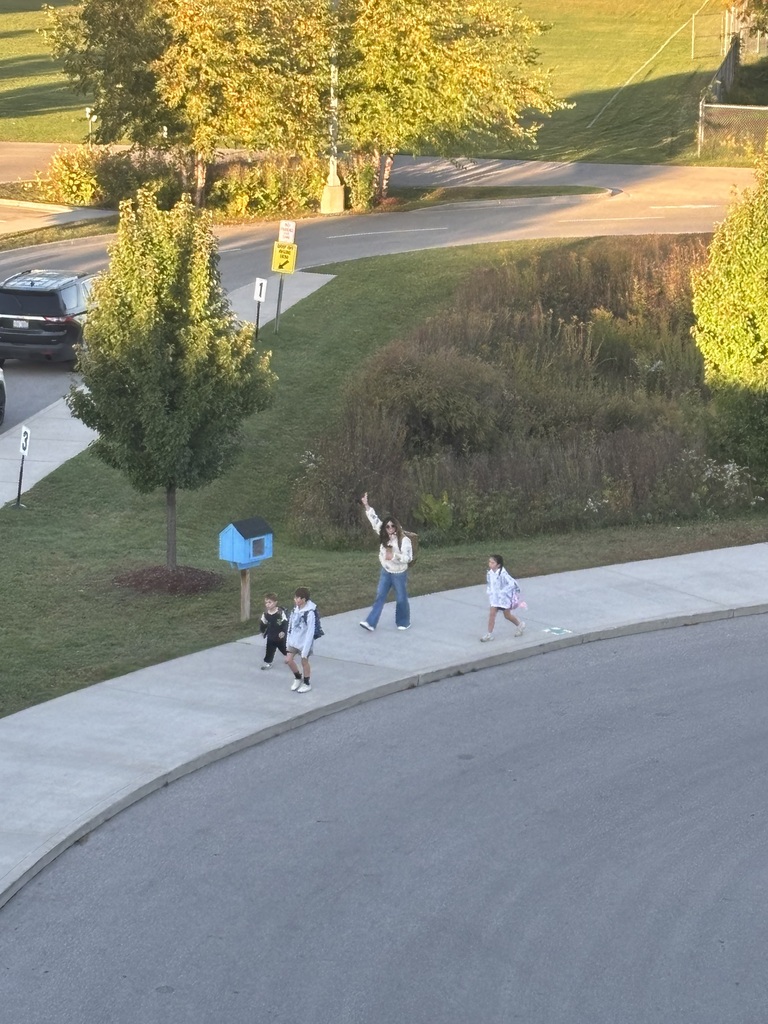 Four people, including two children, walk on a sidewalk. A blue mailbox and a tree stand nearby. A car drives past. The walkers are waving up to Mr. Swegles on the roof.