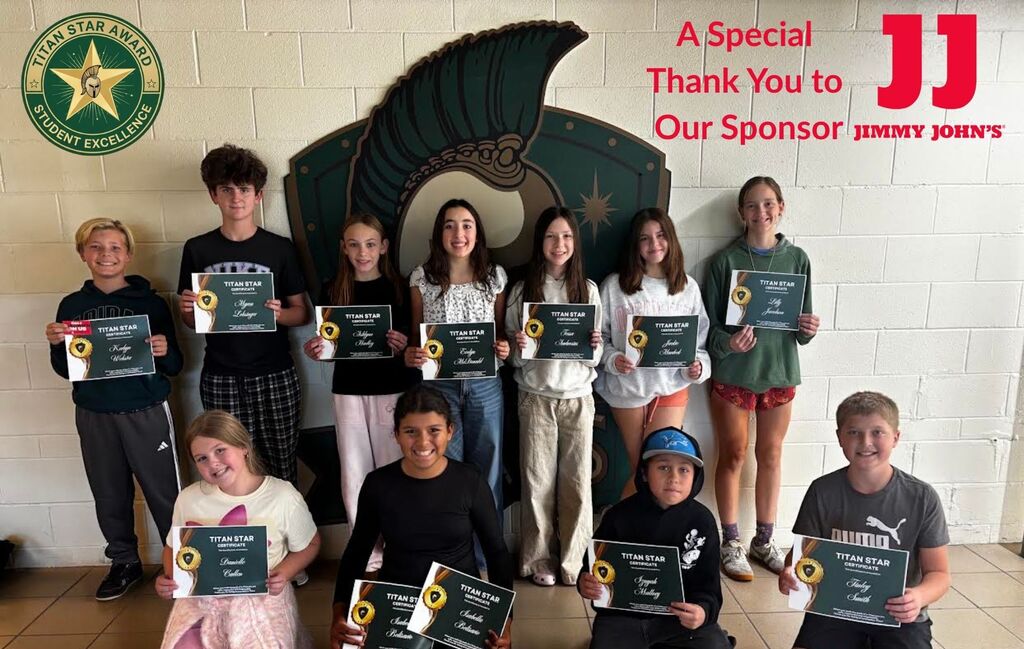 Group of children in a room holding certificates and standing in front of a white wall with a sponsor's logo.