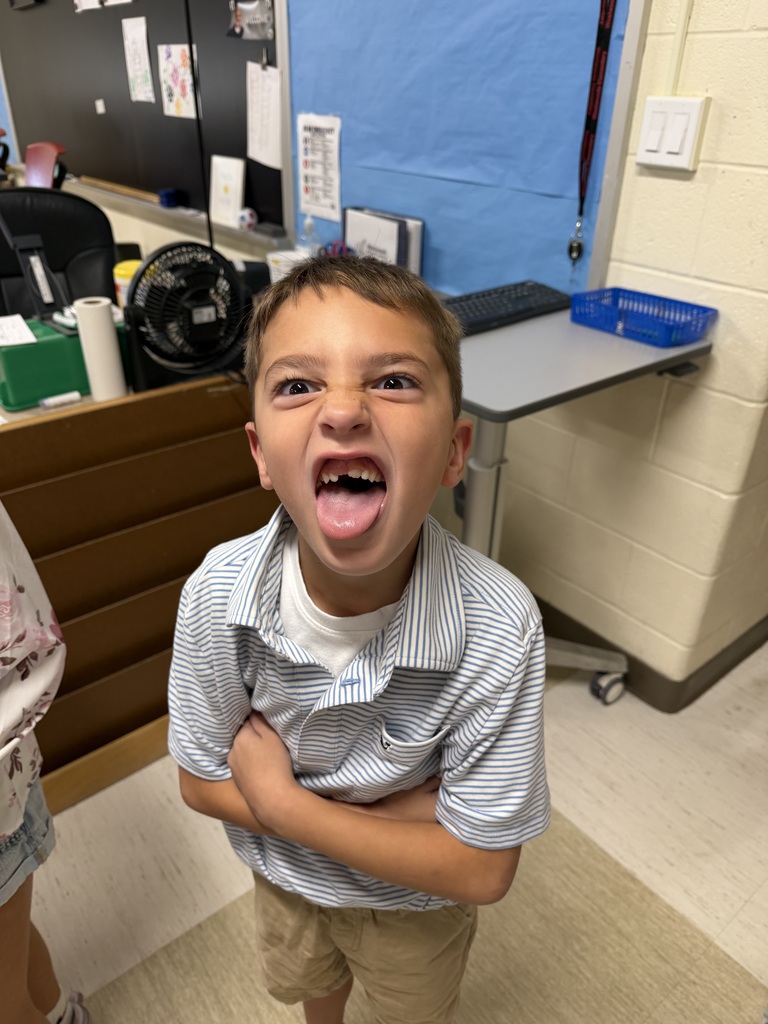 A young boy with his mouth open stands in a classroom with a person nearby.