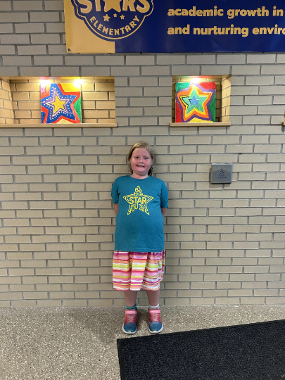 A child stands in front of a brick wall. The wall has two lit star-shaped artworks and a banner.