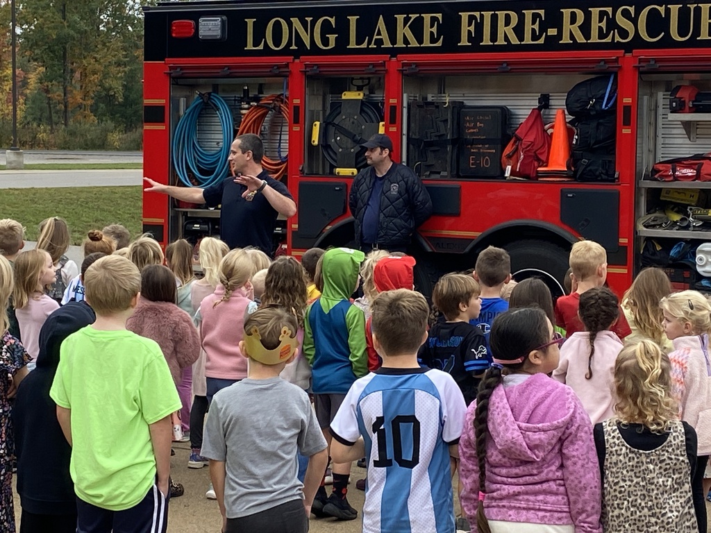 Children gather around a fire truck with two firefighters standing near it. The truck is labeled "Long Lake Fire-Rescue".