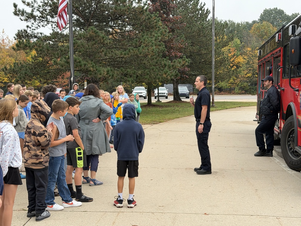 A group of children listening to a fireman in front of a red fire truck.