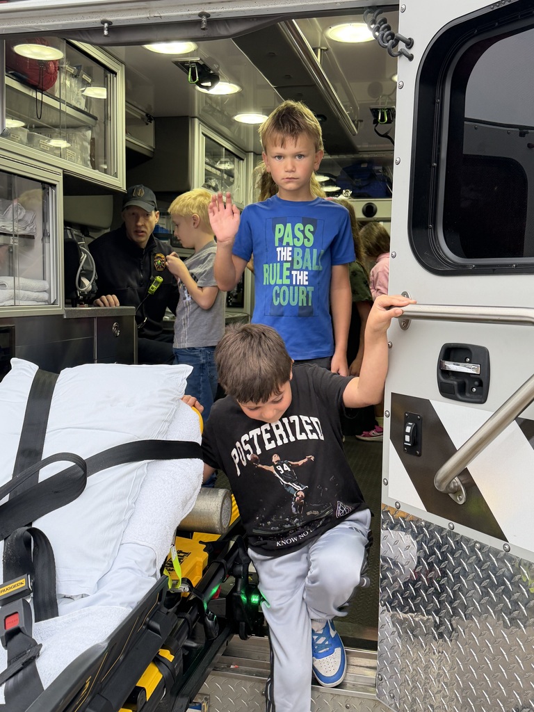 Children are entering an ambulance. A stretcher is inside. A person is waving.