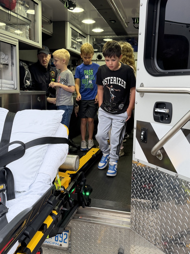 Four children and a man are inside an ambulance. One boy walks out while the others watch.