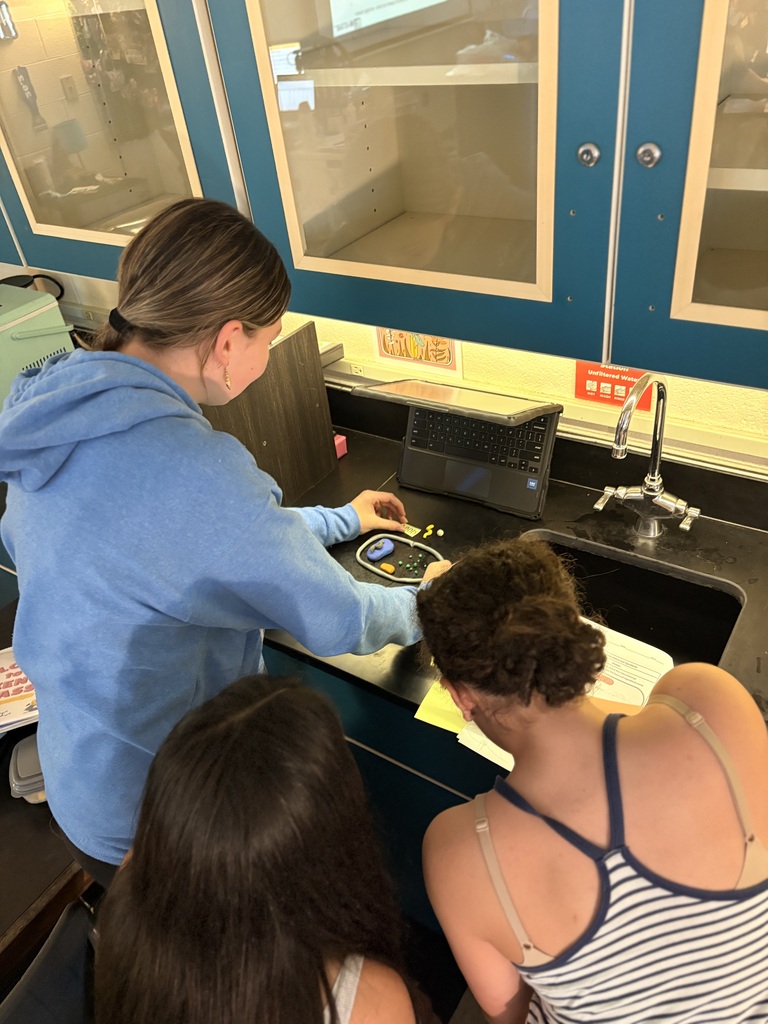 Three individuals are gathered around a countertop, with one using a device. A sink and cabinets are in the background.