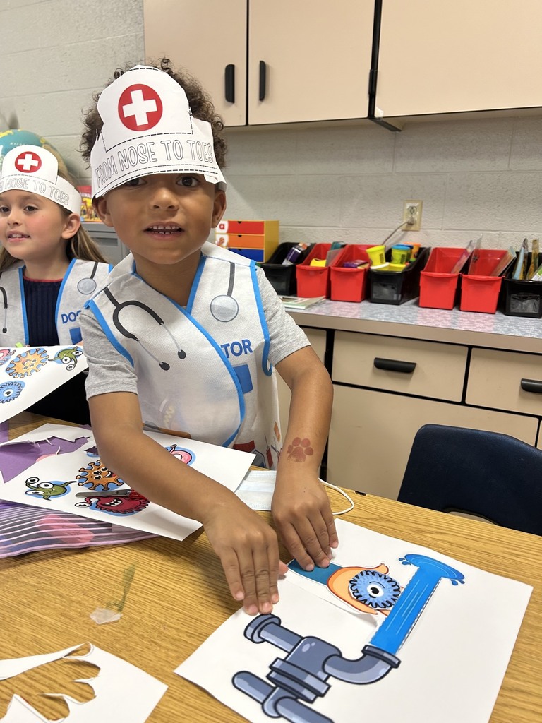 Two children in nurse costumes at a table, one with a stethoscope, the other holding a paper with a wrench.