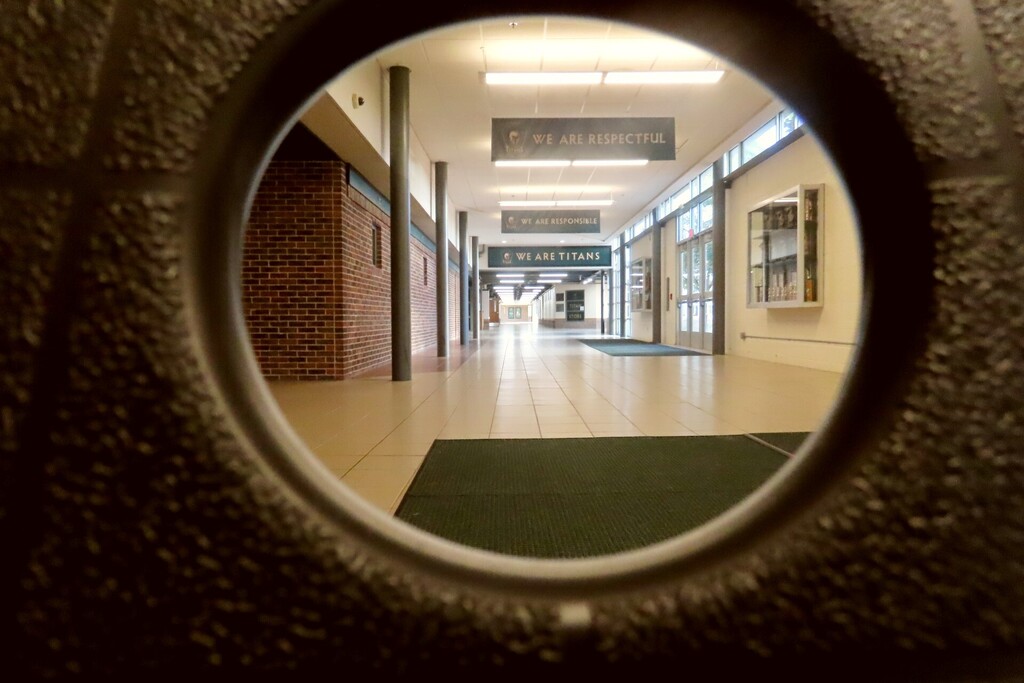 Empty hallway with white floors and brick walls, viewed through a round opening in a wall.