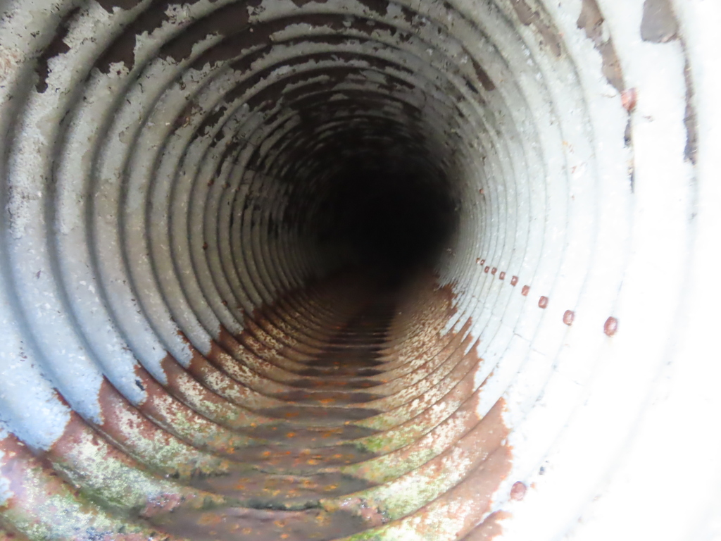 A close view of a spiral-shaped, rusty metal tube with a dark interior and white and brown patches.