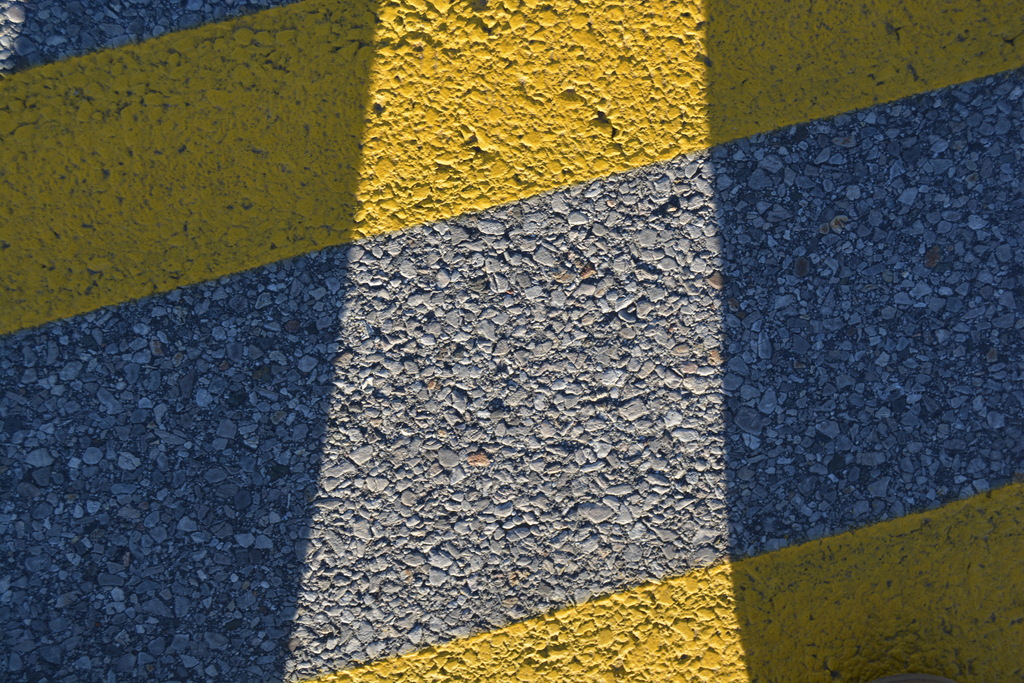 Asphalt surface with yellow and blue markings and shadows, showing a pattern of yellow and blue stripes.
