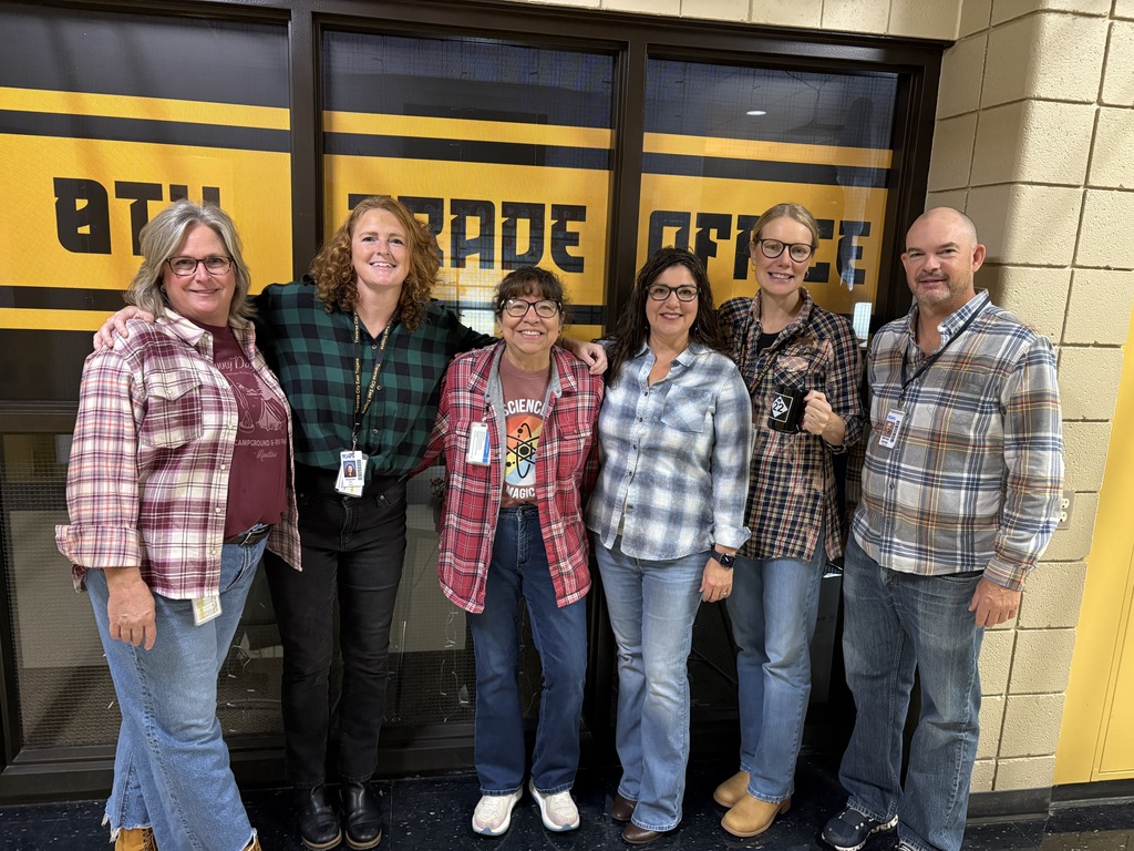 Six adults stand together in front of a yellow and black sign with white text.