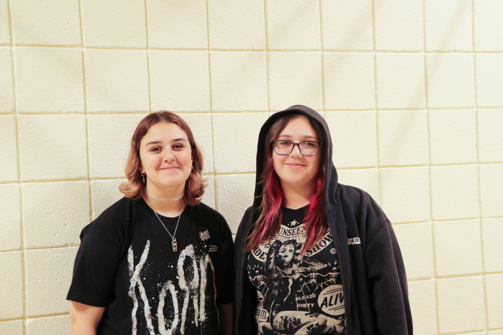Two students standing together, one in a hoodie and the other in a shirt with "Korn" on it.