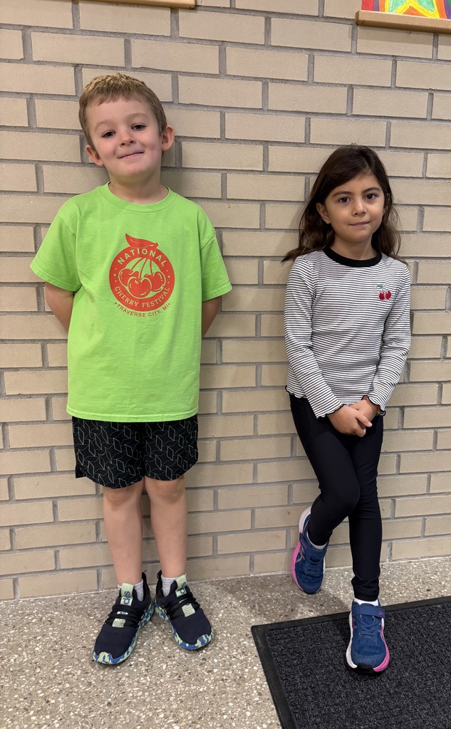 Two children standing next to a wall, a boy in a green shirt and the girl in a gray shirt.
