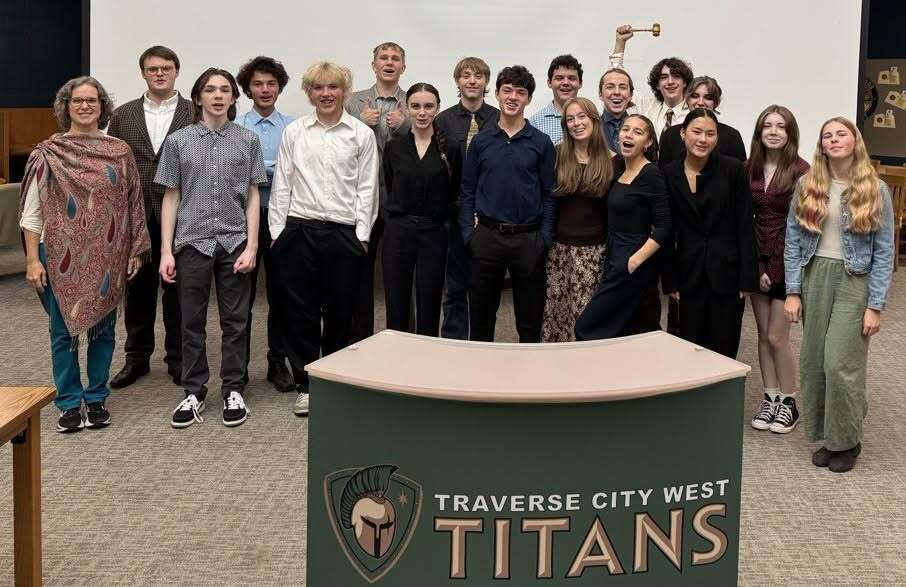 Students and adults stand together in front of a sign that reads "TRAVERSE CITY WEST TITANS."