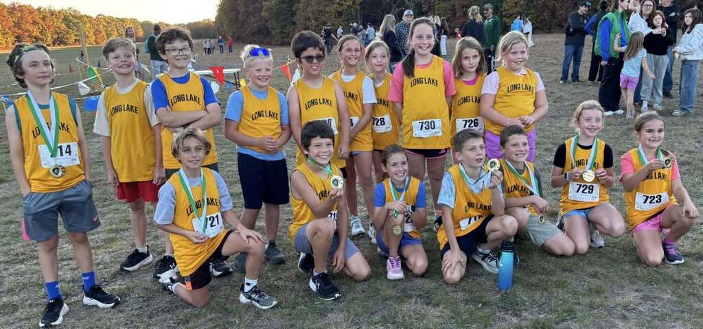 A group of young athletes in matching yellow shirts poses with medals for a photo on a field.