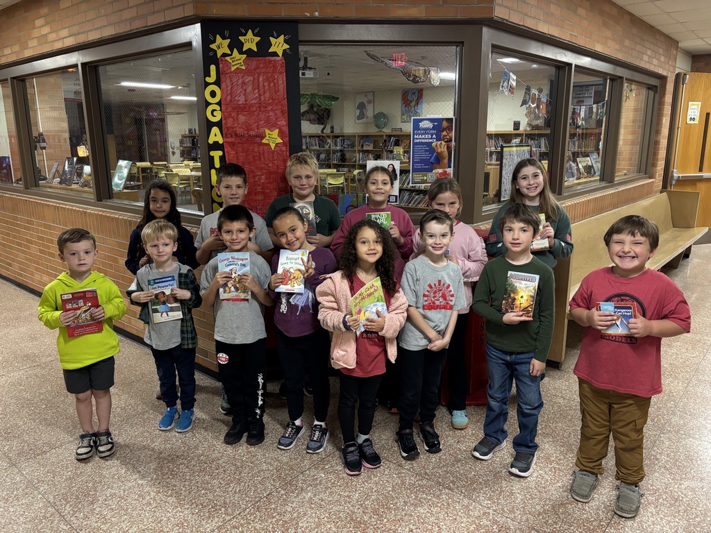 Group of children with books in front of a library display window.