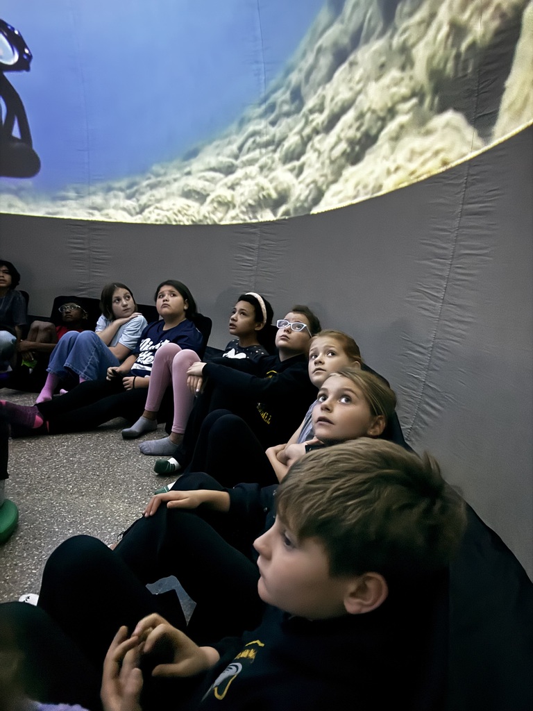 Children seated watching a video projected onto a curved wall with an underwater scene.