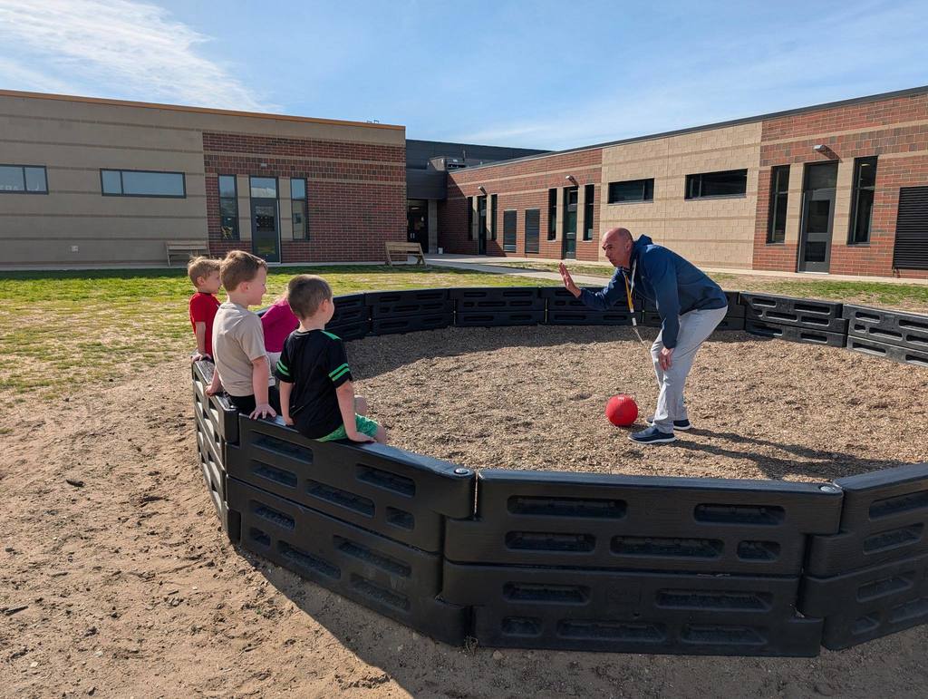 Four preschool students learning about the rules of Gaga ball from Mr. Rykse.