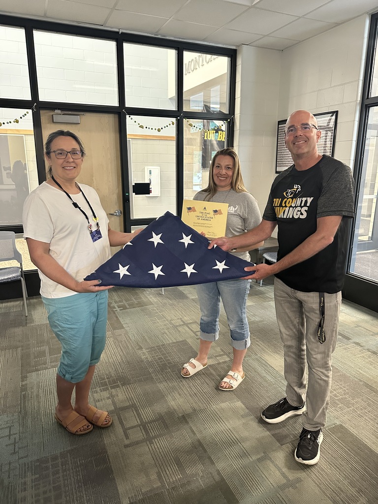 Two principals receiving an American flag from a representative from Kent District Library.