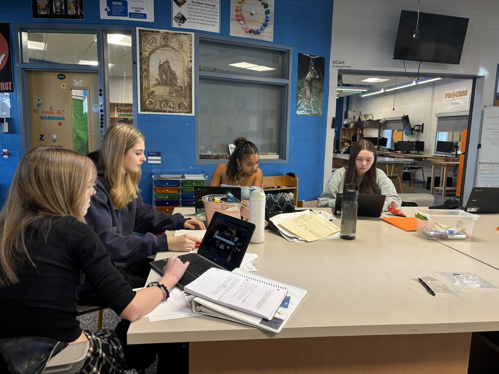 Students editing video on chromebooks while sitting around a work bench table