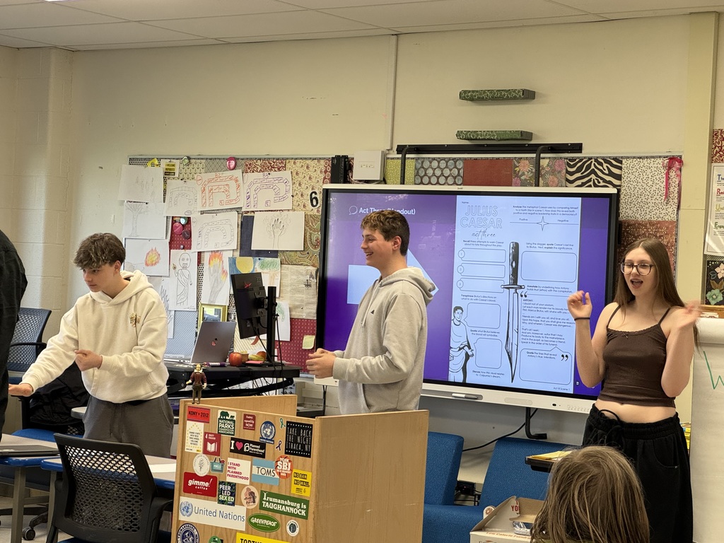 Students smiling with hands in action and a whiteboard showing an image of a dagger and graphic organizer