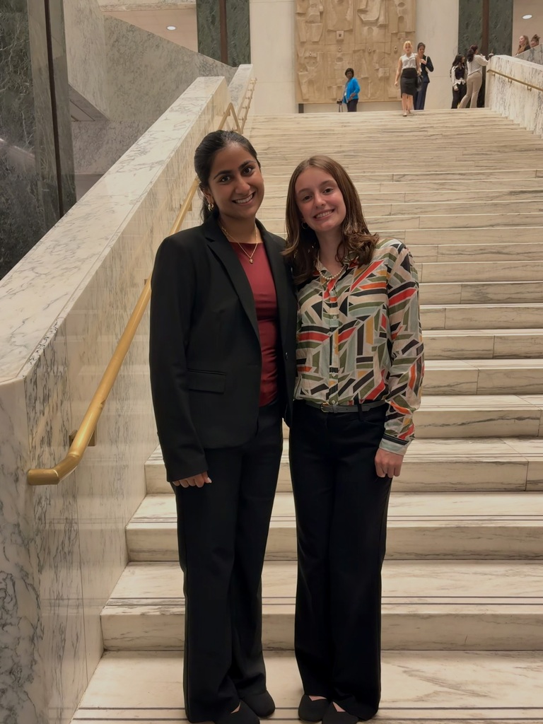 Two smiling individuals in front of marble steps inside the capitol building