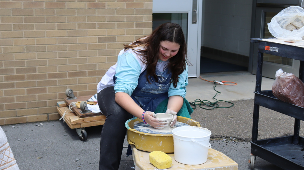 A student smiles while working with a pottery wheel