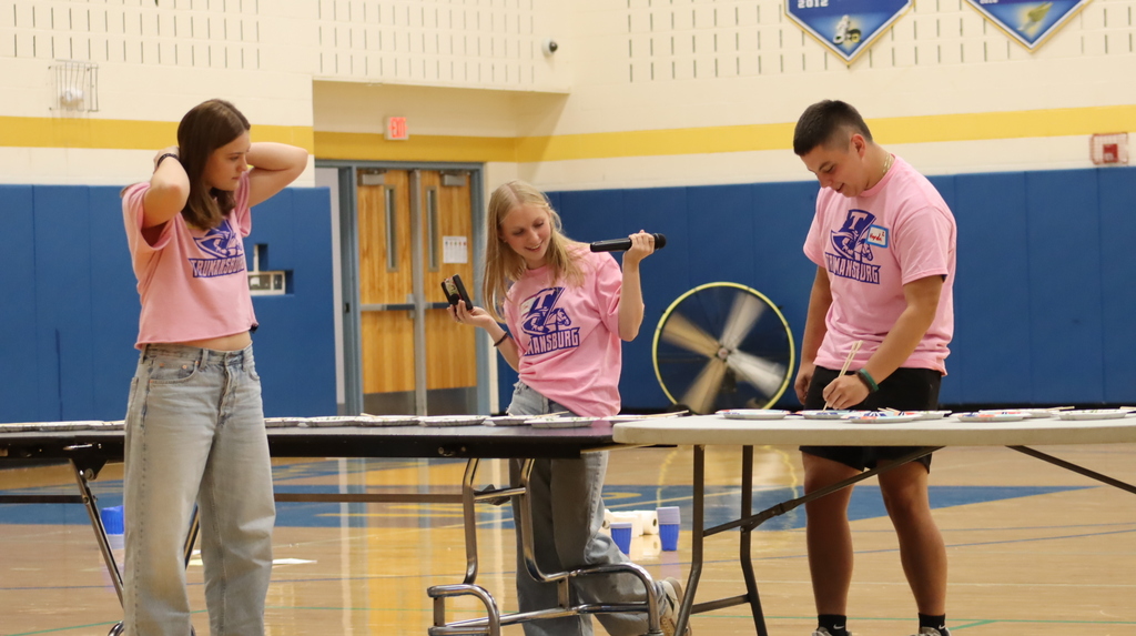 3 students in pink tshirts in a gym with long tables