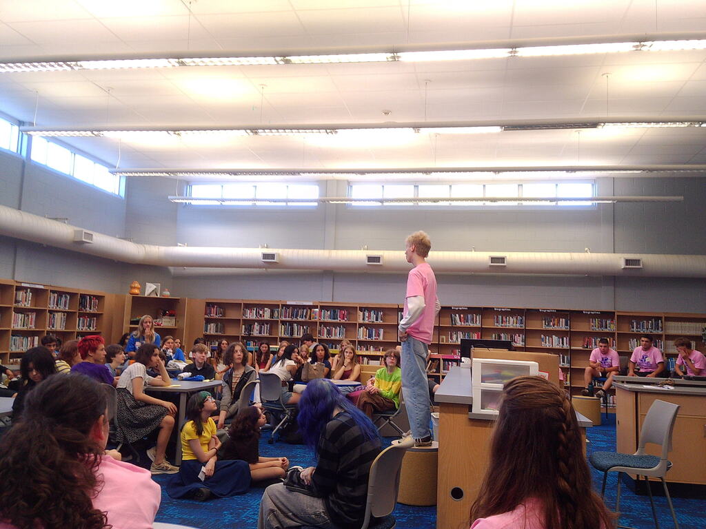 A student standing on a bench in front of other students in a library