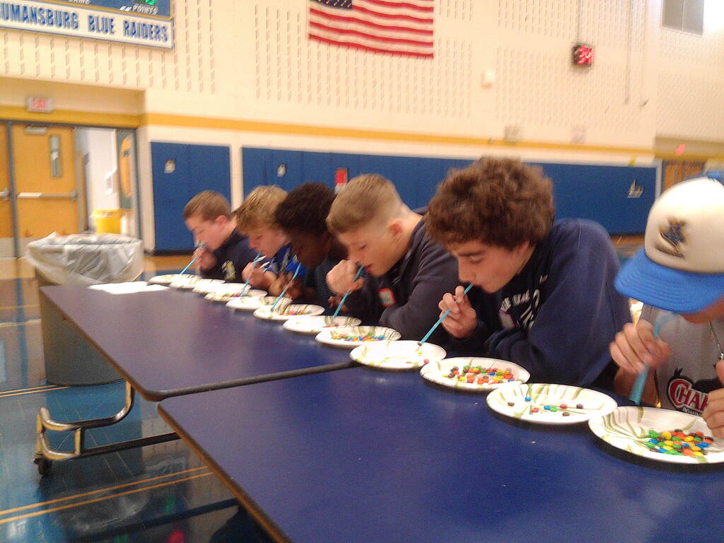 Students with straws blowing on candy pieces in paper plates