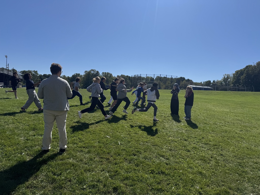 Students running through the grass with a teacher looking on