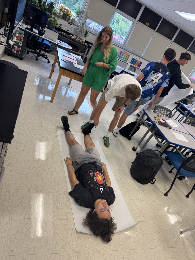 Student laying on a poster on the ground with others in a classroom