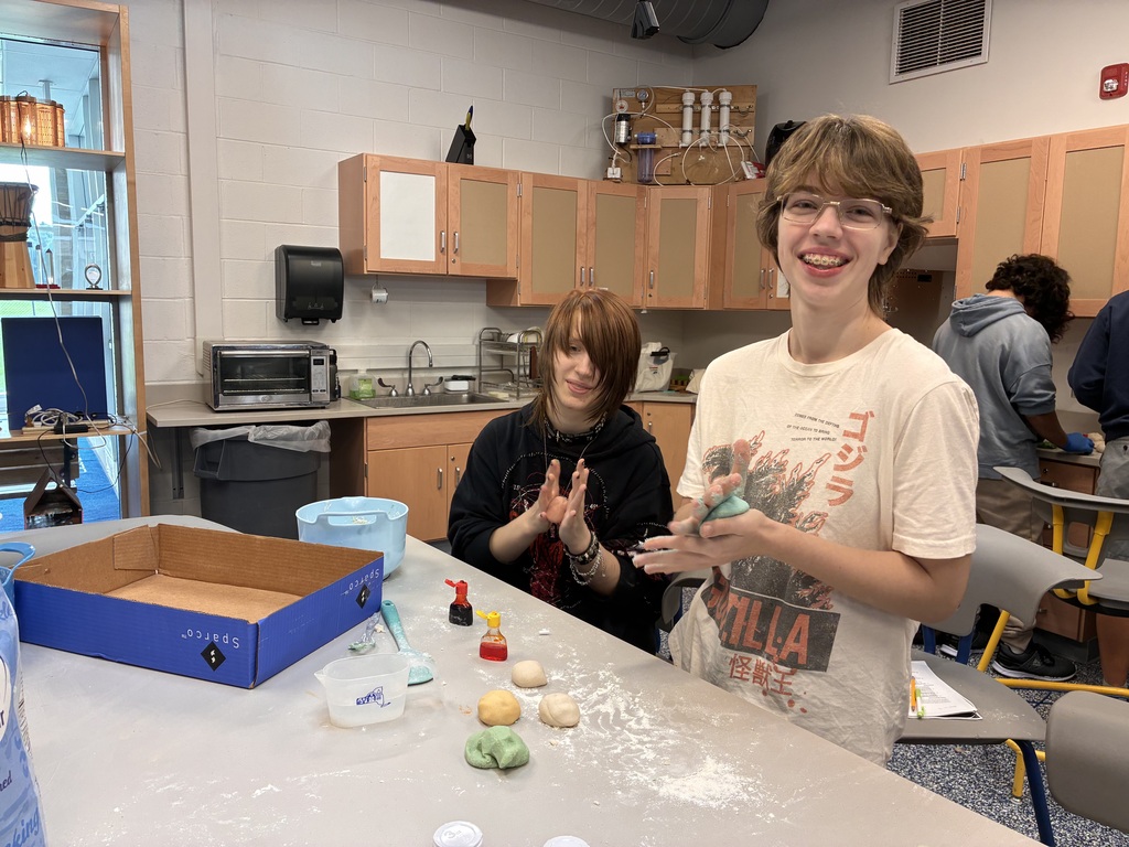 Two students smiling and rolling balls of dough
